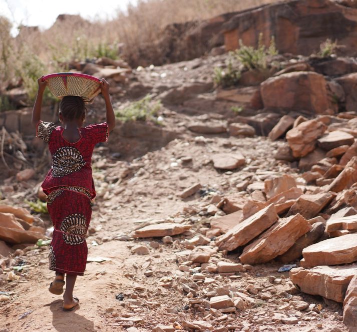 Young child holding basket above their head, walking up a stone pathway