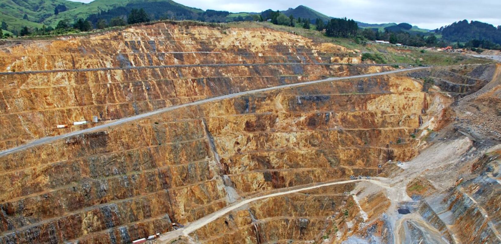 Deep mining quarry, with construction machinery throughout. At the bottom of the quarry lies a small lake of water.