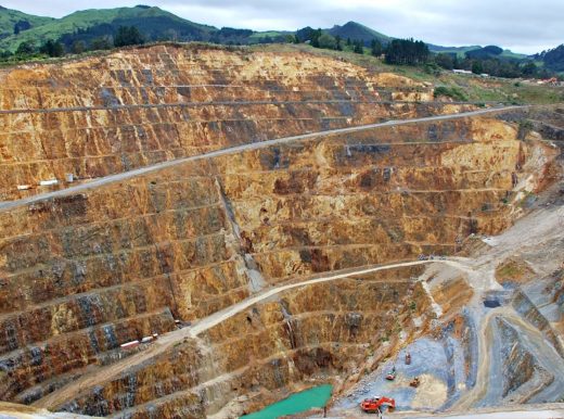 Deep mining quarry, with construction machinery throughout. At the bottom of the quarry lies a small lake of water.