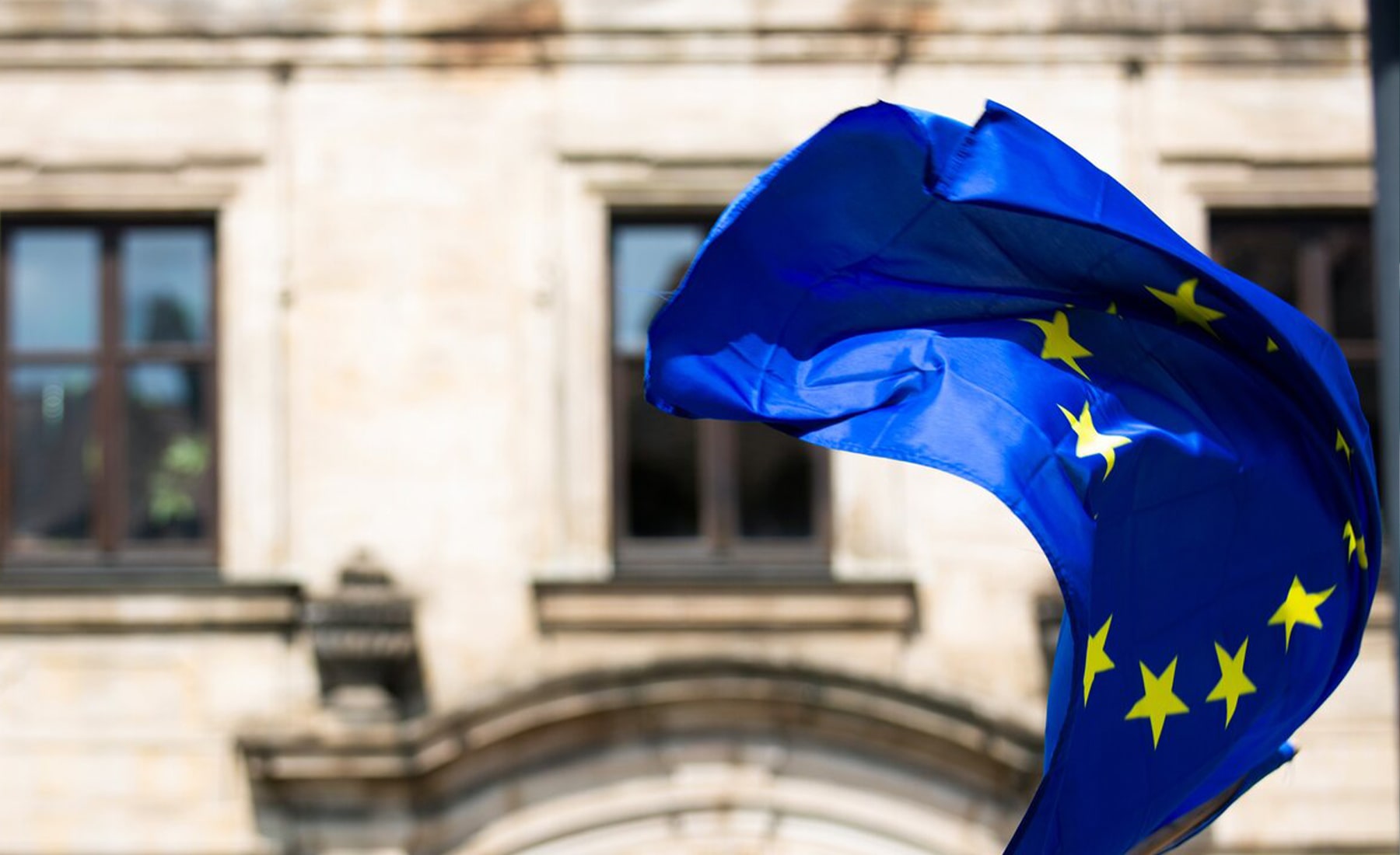 European Union flag blowing in the air, with a building in the background