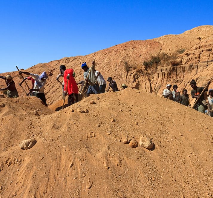 Large pile of dirt and rocks, with workers digging through and mining