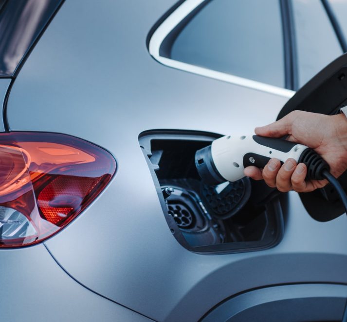 Hand plugging in electric plug into the charging port of the electric car