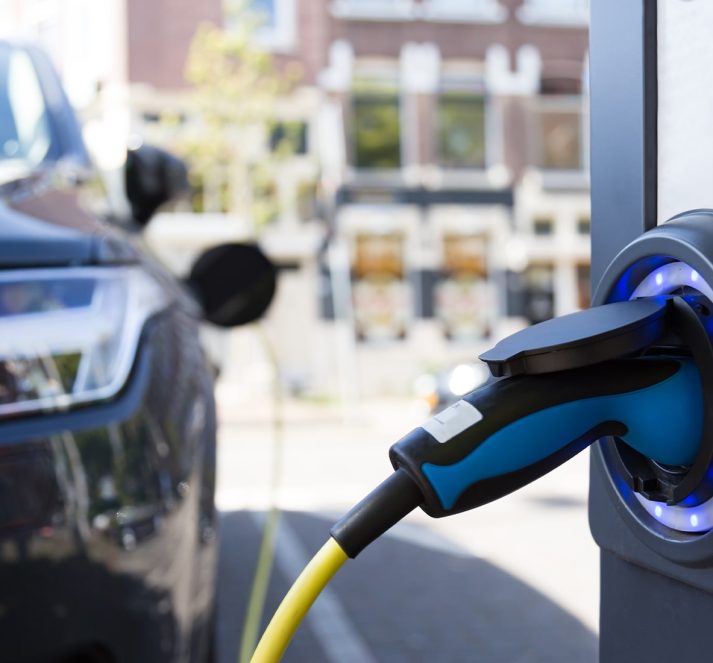 Car in the background parked at charging point, with charging port plugged in, in the foreground