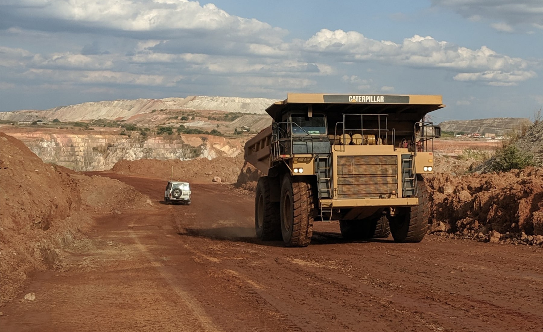 Caterpillar heavy truck driving across dirt road, with mining quarries in the background