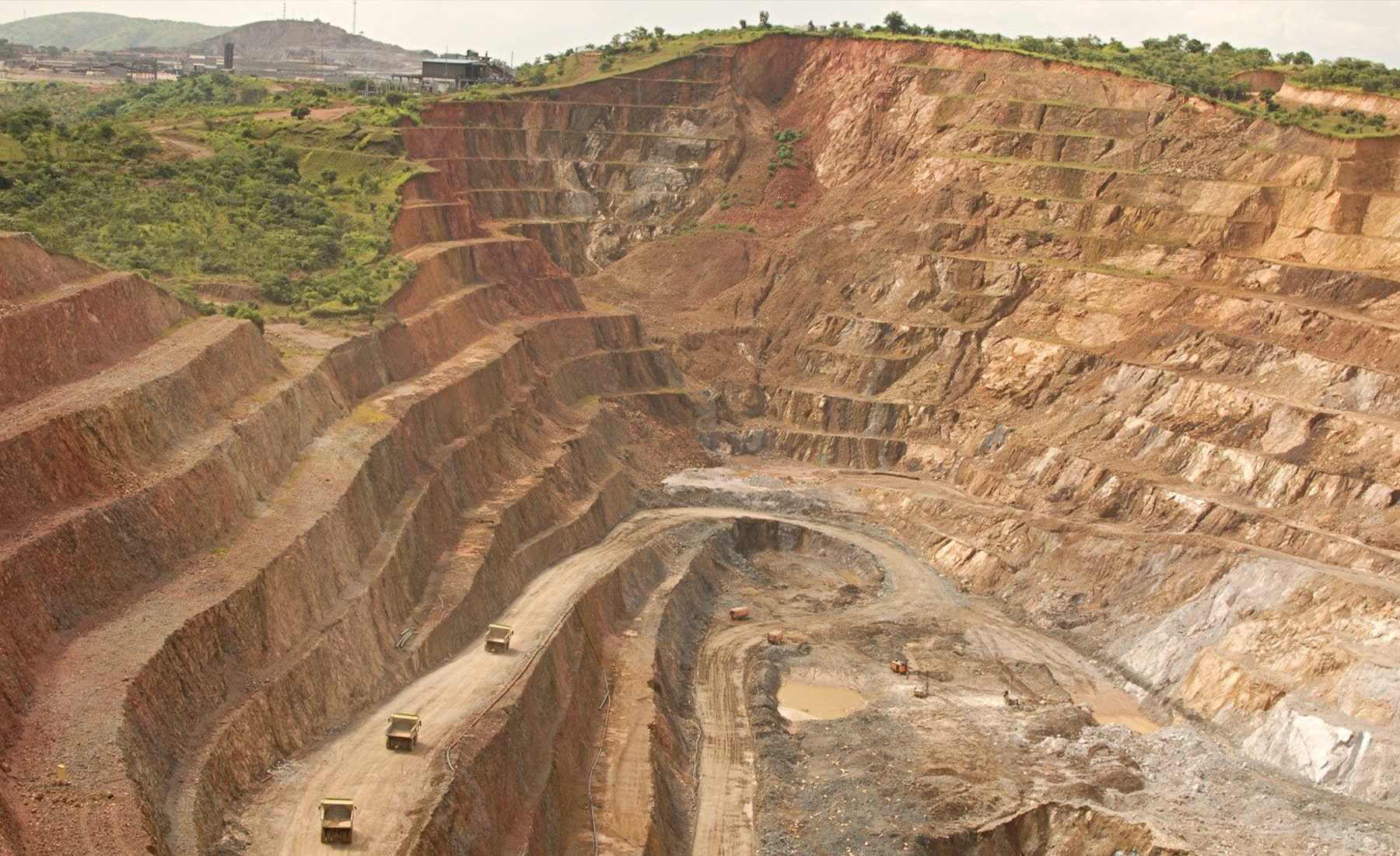 Caterpillar heavy truck driving across dirt road, with mining quarries in the background