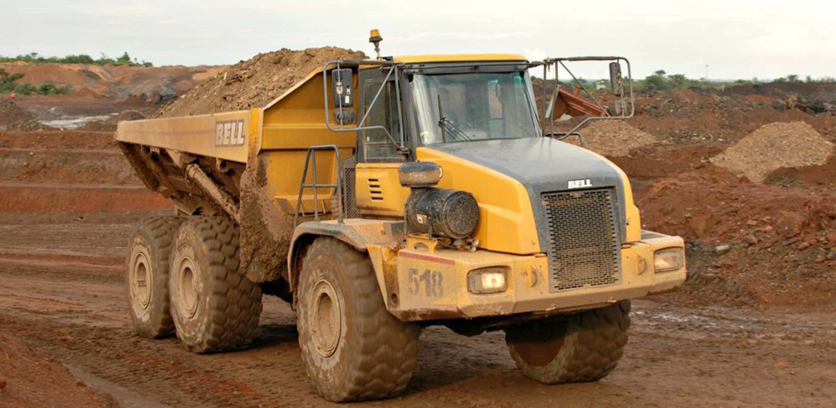 Yellow heavy duty truck, carrying materials in the back along a dirt road