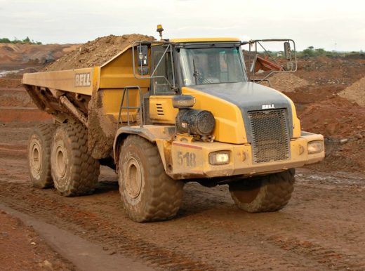 Yellow heavy duty truck, carrying materials in the back along a dirt road