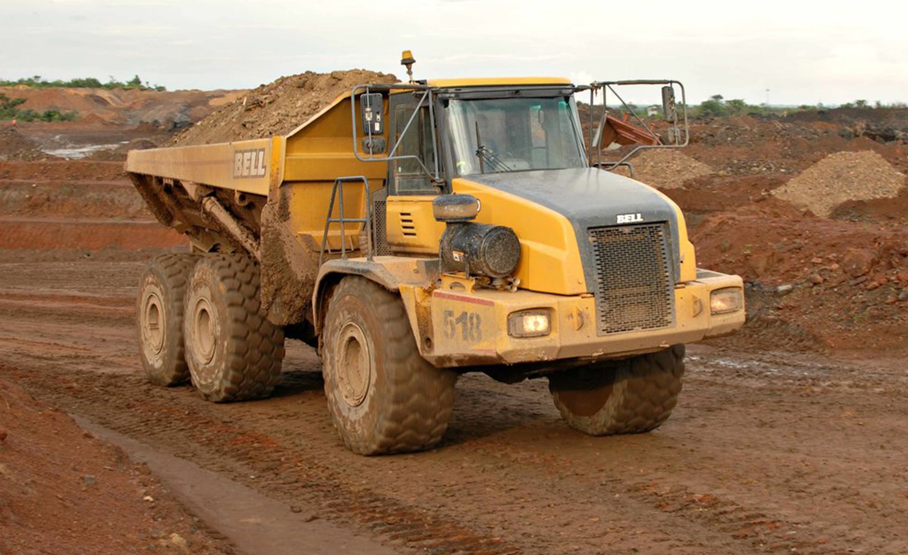 Yellow heavy duty truck, carrying materials in the back along a dirt road