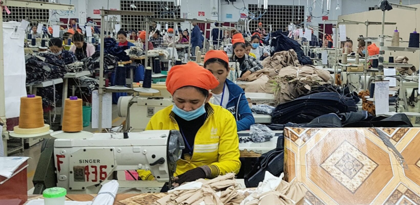 Clothing factor, with a woman wearing a face mask, whilst using a sewing machine at her desk