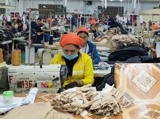 Clothing factor, with a woman wearing a face mask, whilst using a sewing machine at her desk