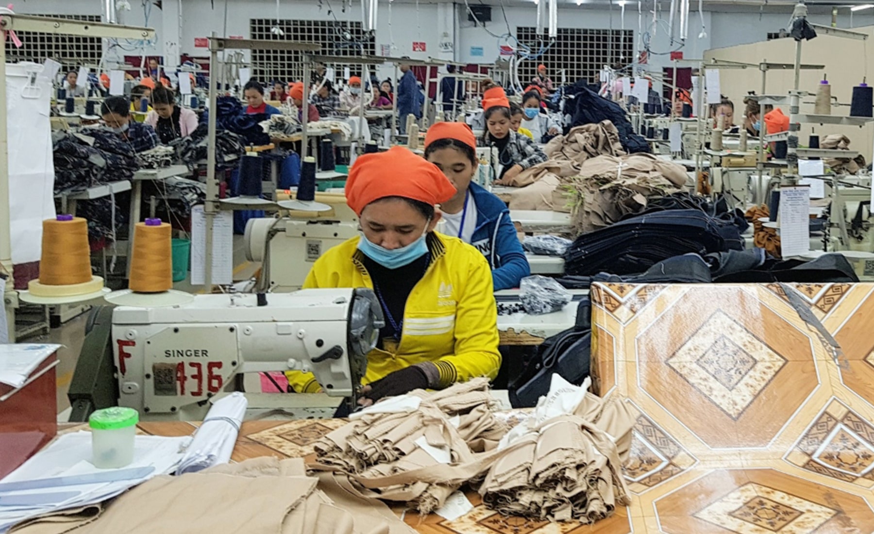 Clothing factor, with a woman wearing a face mask, whilst using a sewing machine at her desk